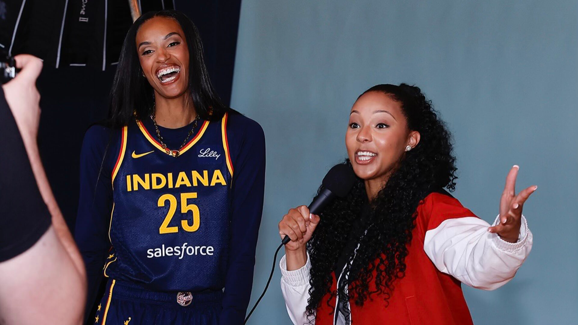 Olivia West gestures excitedly while holding a mic and speaking to Indiana Fever point guard Dewanna Bonner.