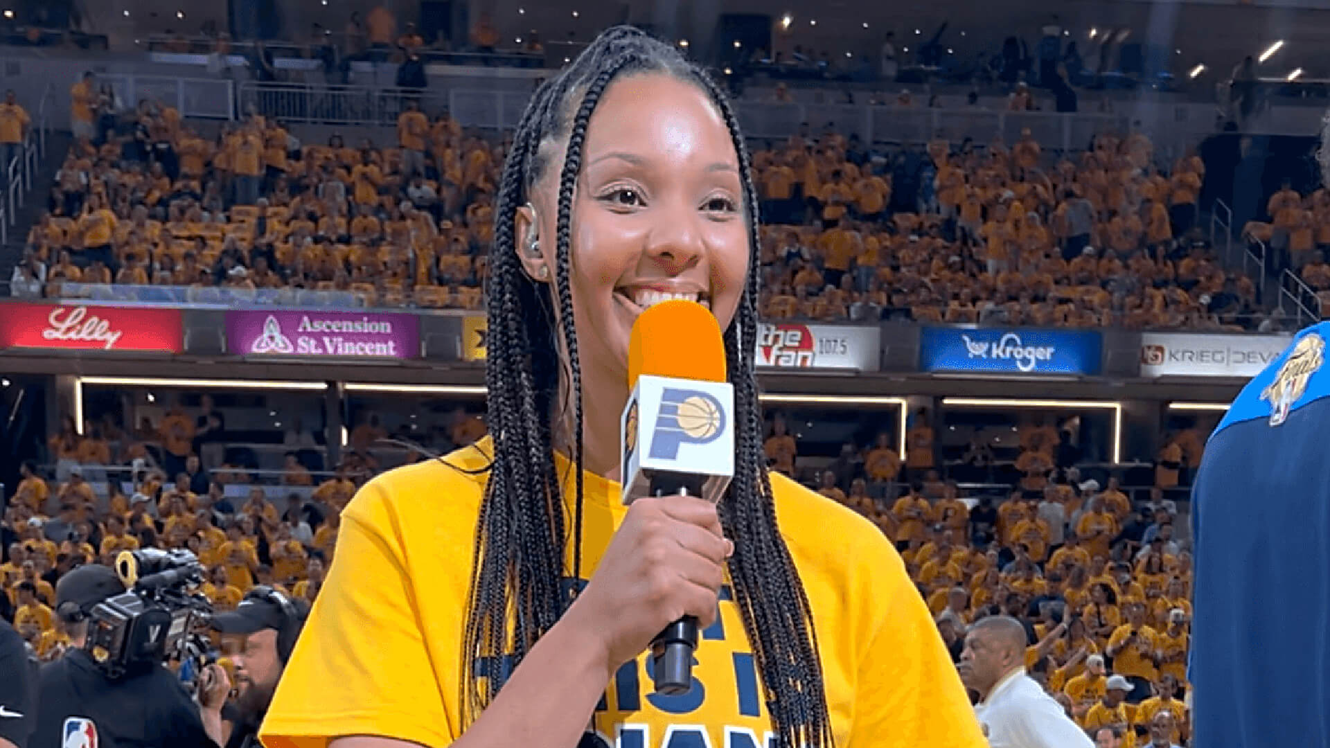 Olivia West holds a mic and poses and smiles for the camera at Gainbridge Fieldhouse.