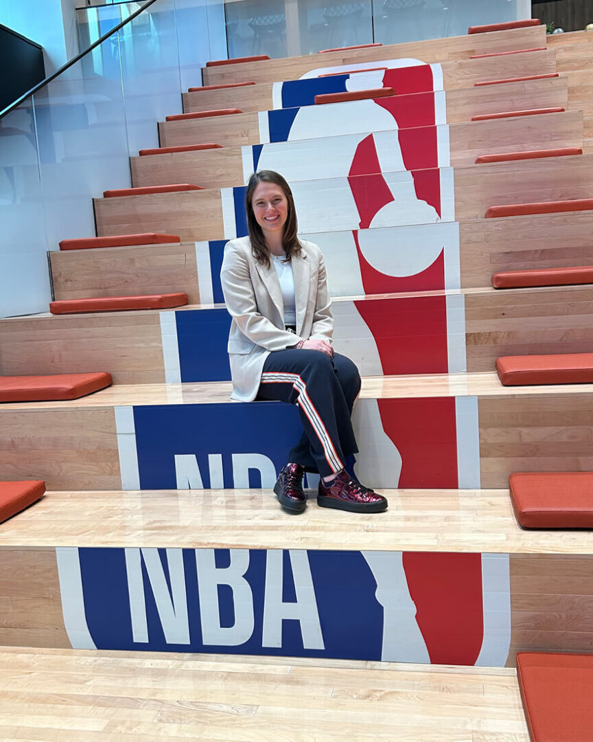 Léony Boudreau sits on a row of bleachers that feature the NBA logo