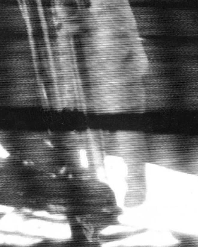 Black-and-white TV image of Neil Armstrong descending a ladder onto the lunar surface