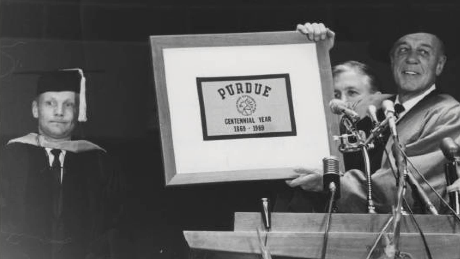 Purdue President Frederick Hovde holds up a Purdue flag that Boilermaker astronaut Neil Armstrong carried to the moon during the Apollo 11 mission