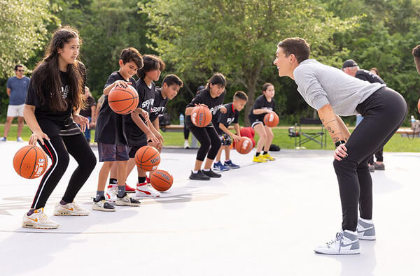 Kara Allen bends over to eye level with a girl dribbling a basketball.