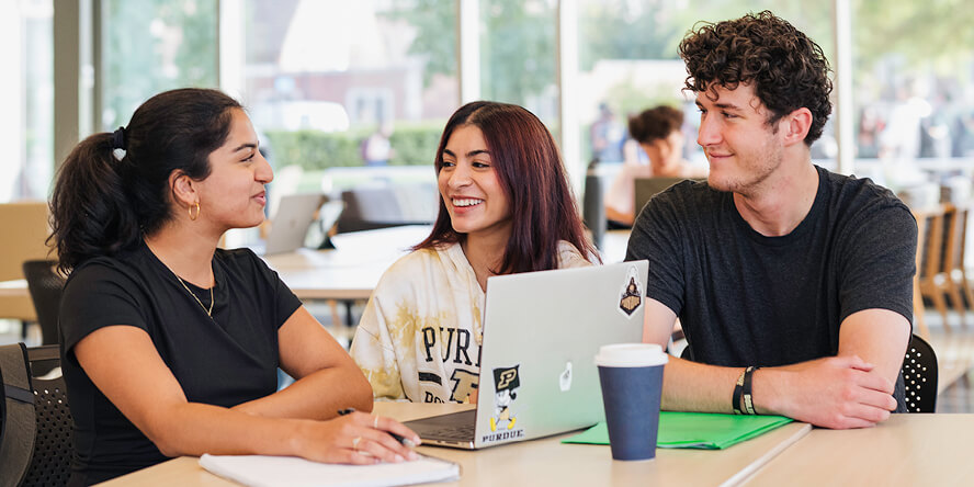 Janvi Prasad sits with friends at a table and has an open laptop.