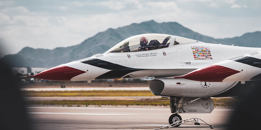 A pilot in a jet on a tarmac with a mountain range in the background.