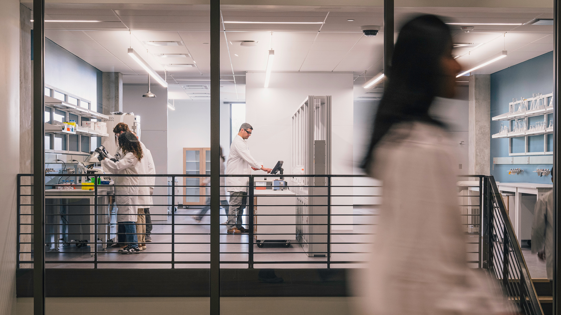 A view of scientists in lab coats using equipment inside a shared research lab at the One Health Innovation District.