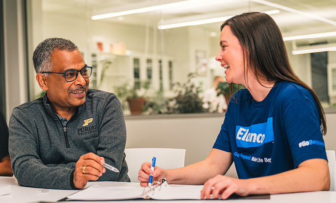Professor Ramaswamy Subramanian and an Elanco colleague sit at a table discussing work over open notes in a collaborative meeting space.