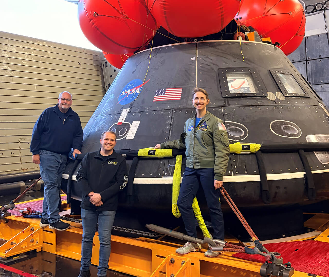 Purdue alumni Rob Lantz, Jason Endsley and Emily Spreen stand next to a practice Orion crew module