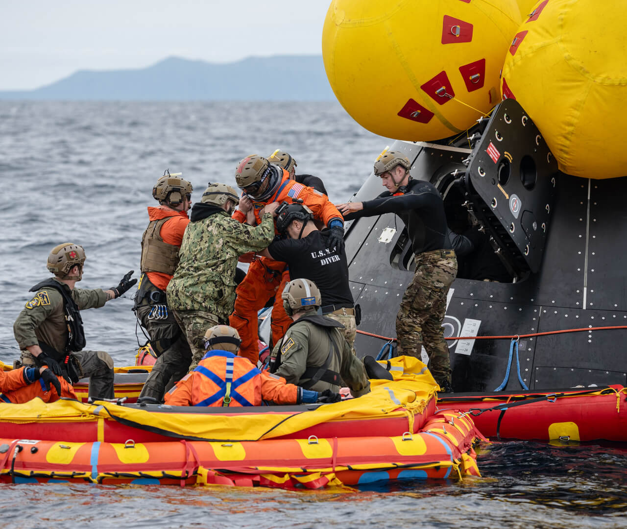 The recovery team practices helping astronauts exit the crew module onto an inflatable floating platform