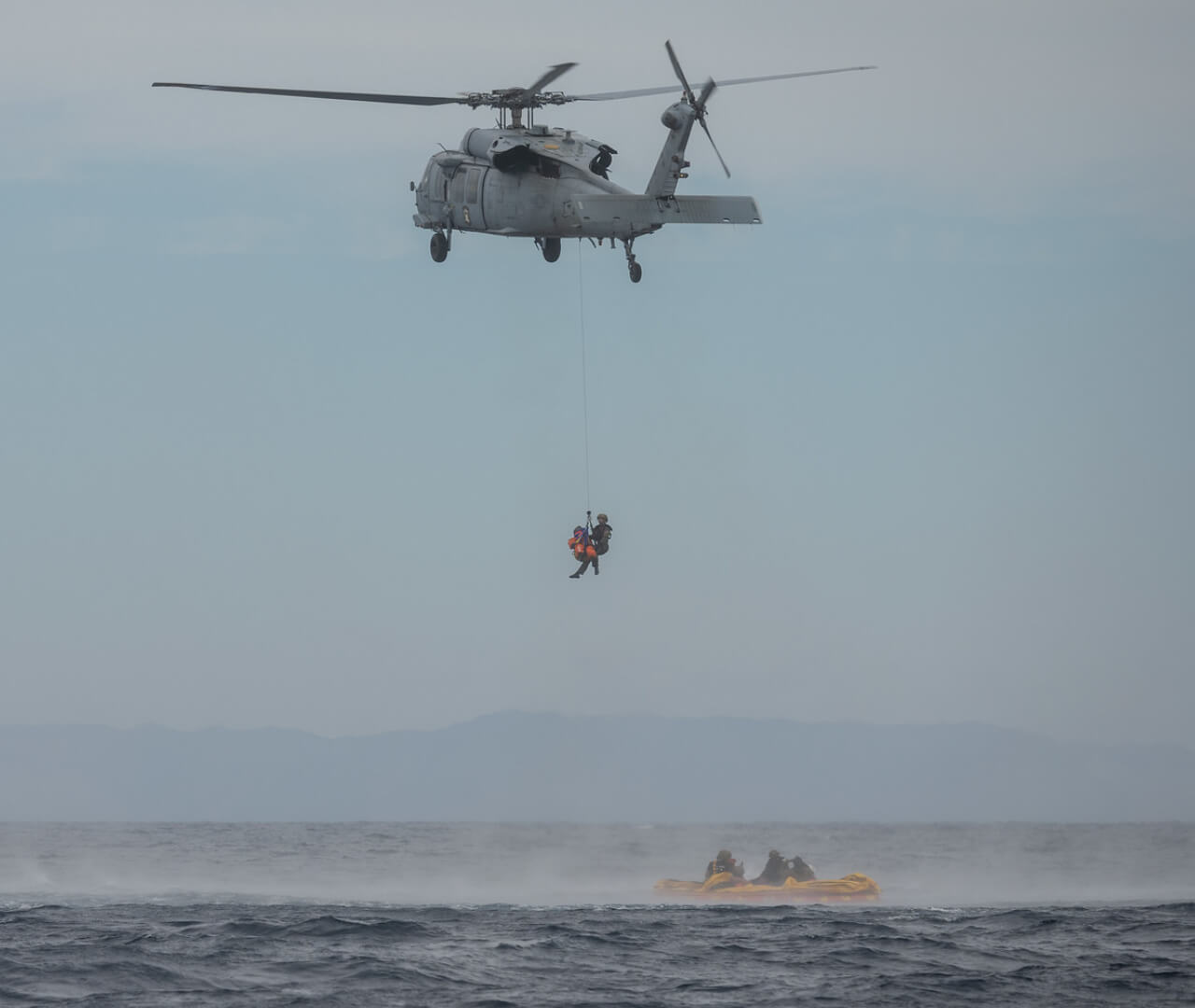 A recovery helicopter practices transporting astronauts from the ocean to a Navy ship during a training session