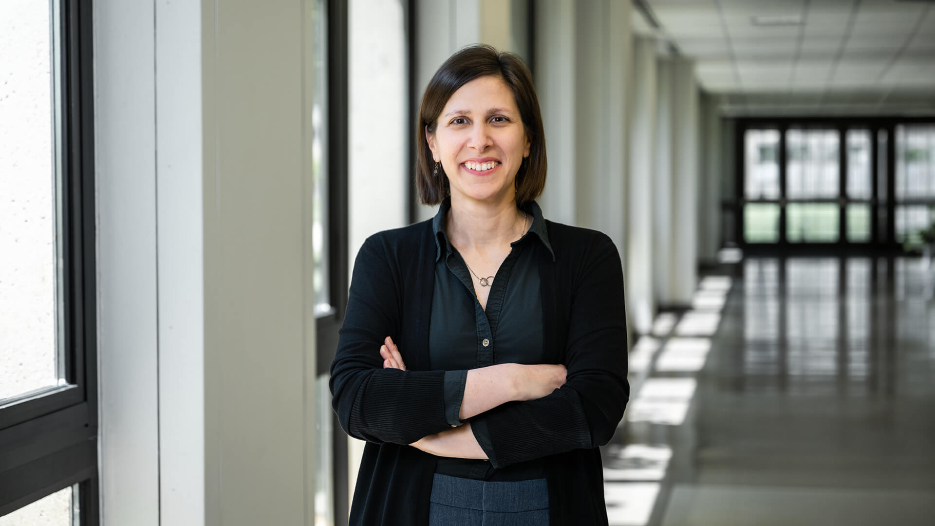 Sharon Miller stands with arms folded in an academic building.