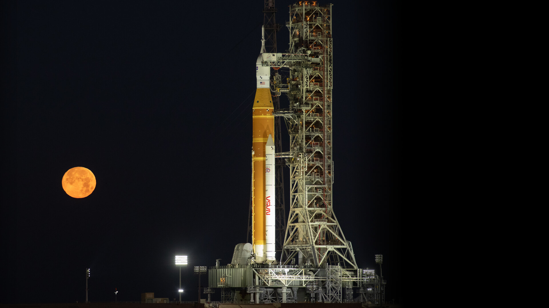 NASA Space Launch System rocket on the launchpad at night with a full moon in the background.
