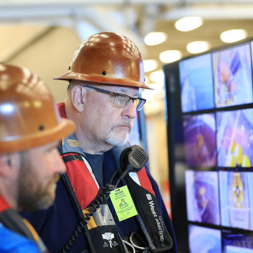 Wearing a hard hat, Rob Lantz looks on during the landing and recovery team’s operations in the Pacific Ocean 