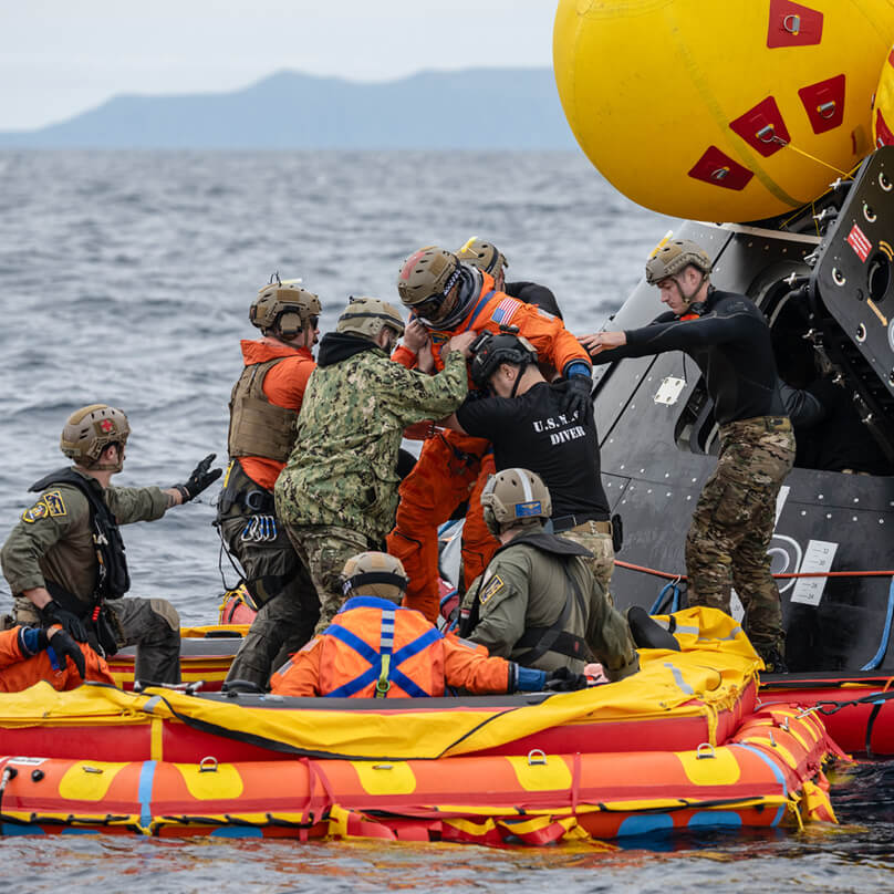 Members of the landing and recovery team assist astronauts as they disembark from the Orion capsule during a water recovery in the Pacific Ocean 