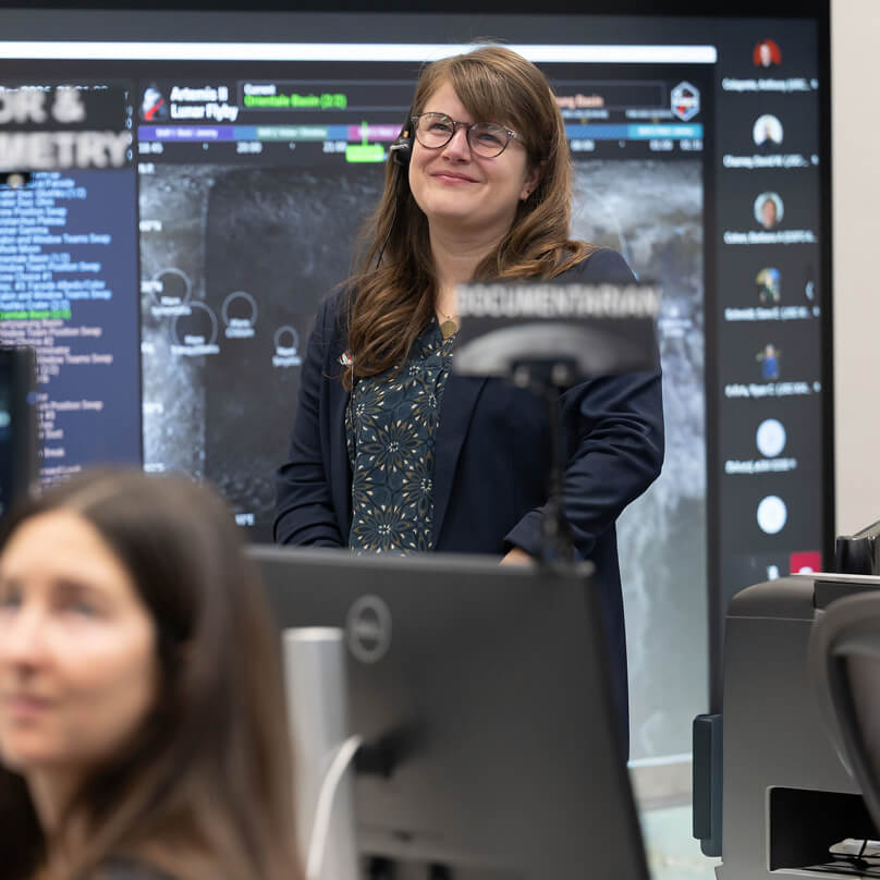 Marie Henderson, standing, and fellow members of the Artemis lunar science team listen as the Artemis II crew shares observations during the lunar flyby 