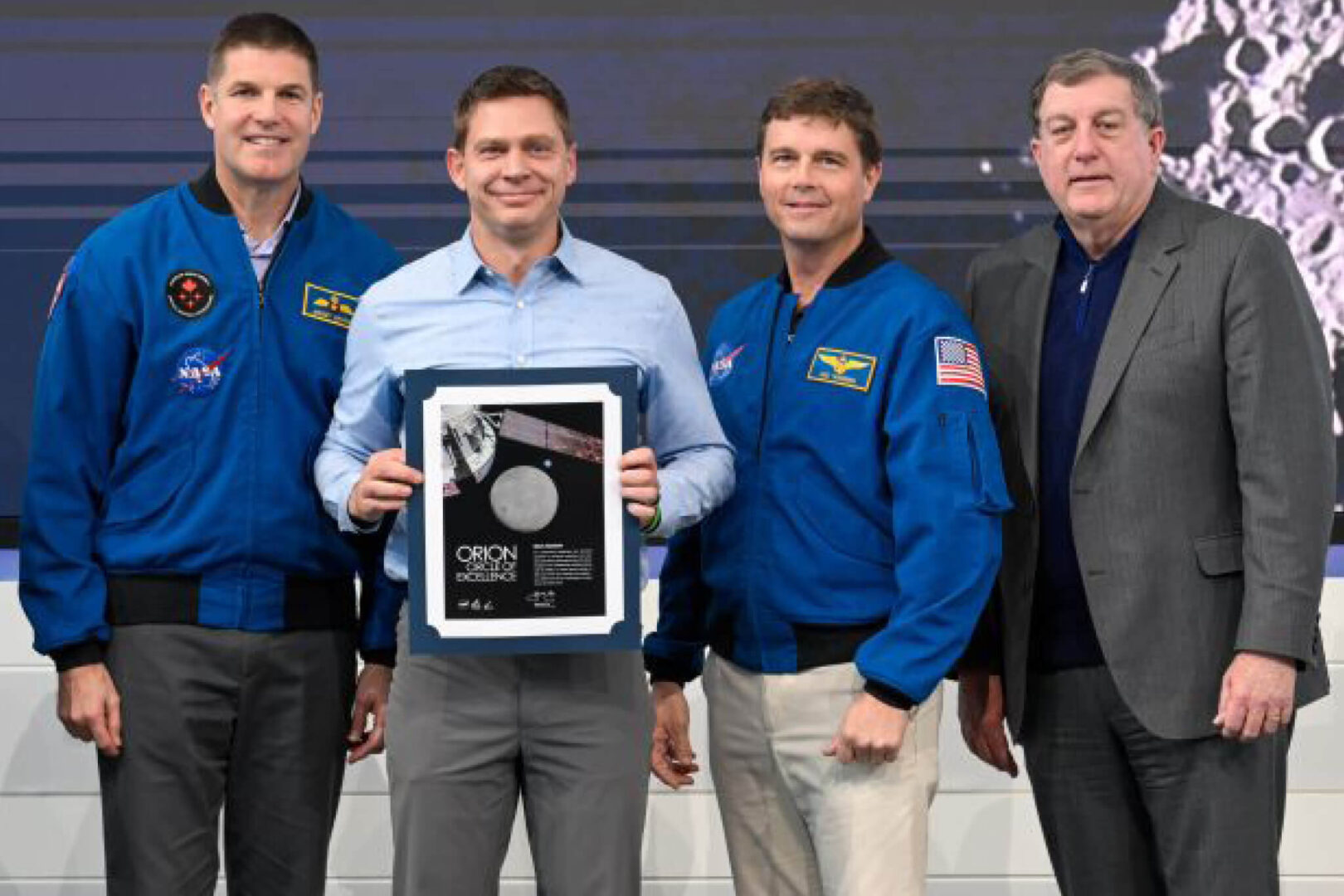 Artemis II astronauts Jeremy Hansen and Reid Wiseman stand on either side of Mark Baldwin, along with Lockheed Martin Vice President of Lunar Exploration Kirk Shireman, as they recognize Baldwin as part of the Orion Circle of Excellence 