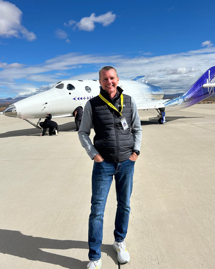 Jason Williamson stands in front of Virgin Galactic’s VSS Unity spacecraft while attending a launch at Spaceport America