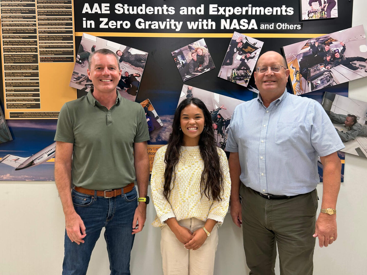 Purdue 1 crew members Jason Williamson, Abigail Mizzi and Steven Collicott pose for a photo in front of a display spotlighting Purdue students’ zero-gravity experiments