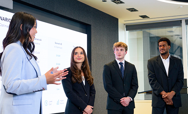 Two female Purdue students and two male Purdue students wearing business attire presenting information from a PowerPoint.