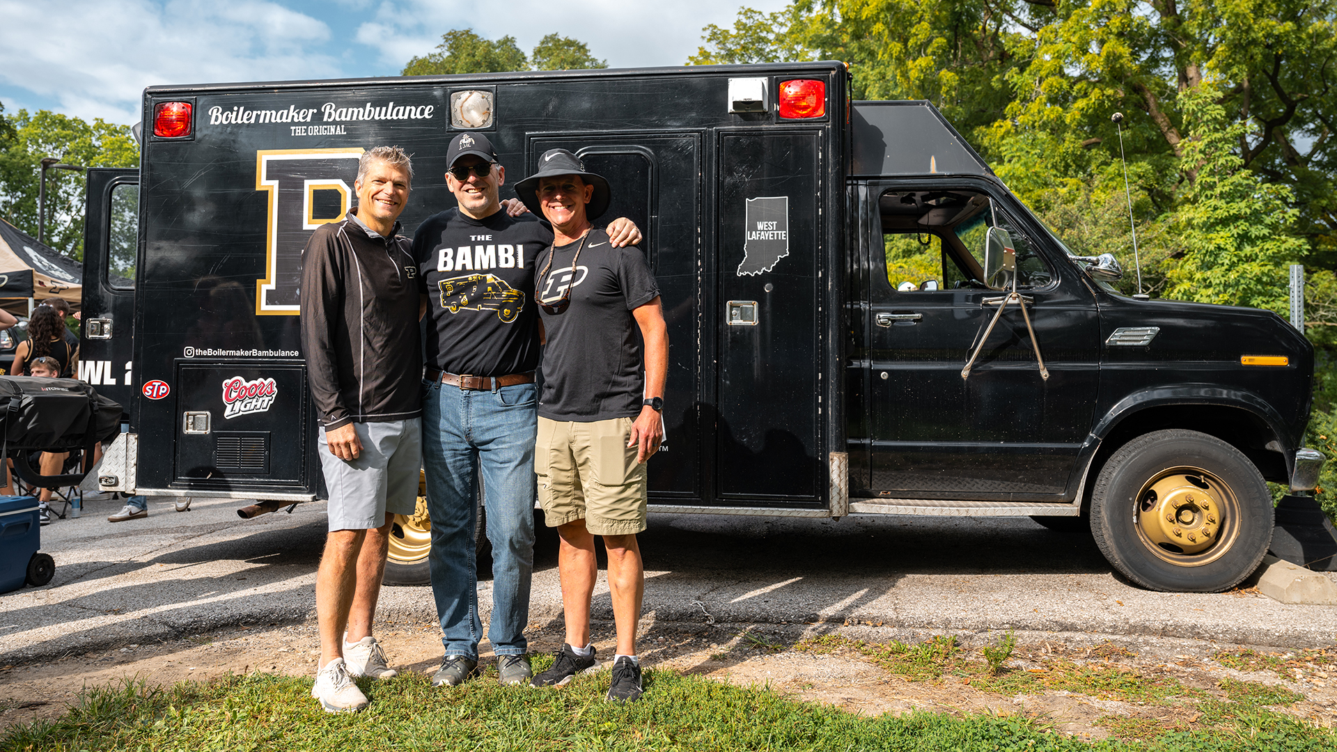 Three people standing by the side of the ambulance.