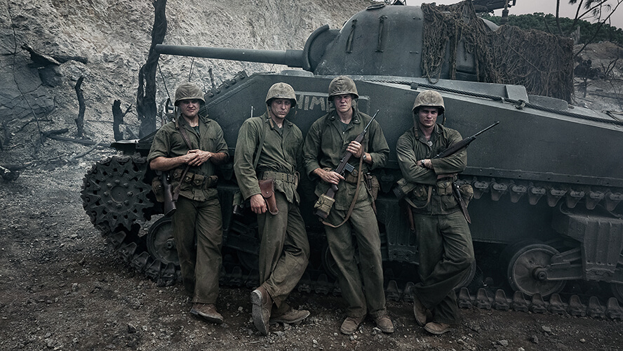 Actors Ray Nicholson, Tom Francis, Bill Skarsgård and Nicholas Galitzine stand in front of a tank in a publicity photo from the set of “The Mosquito Bowl.” 