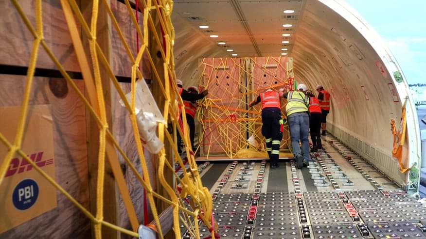 Group of workers pushes crates to the back of plane. 