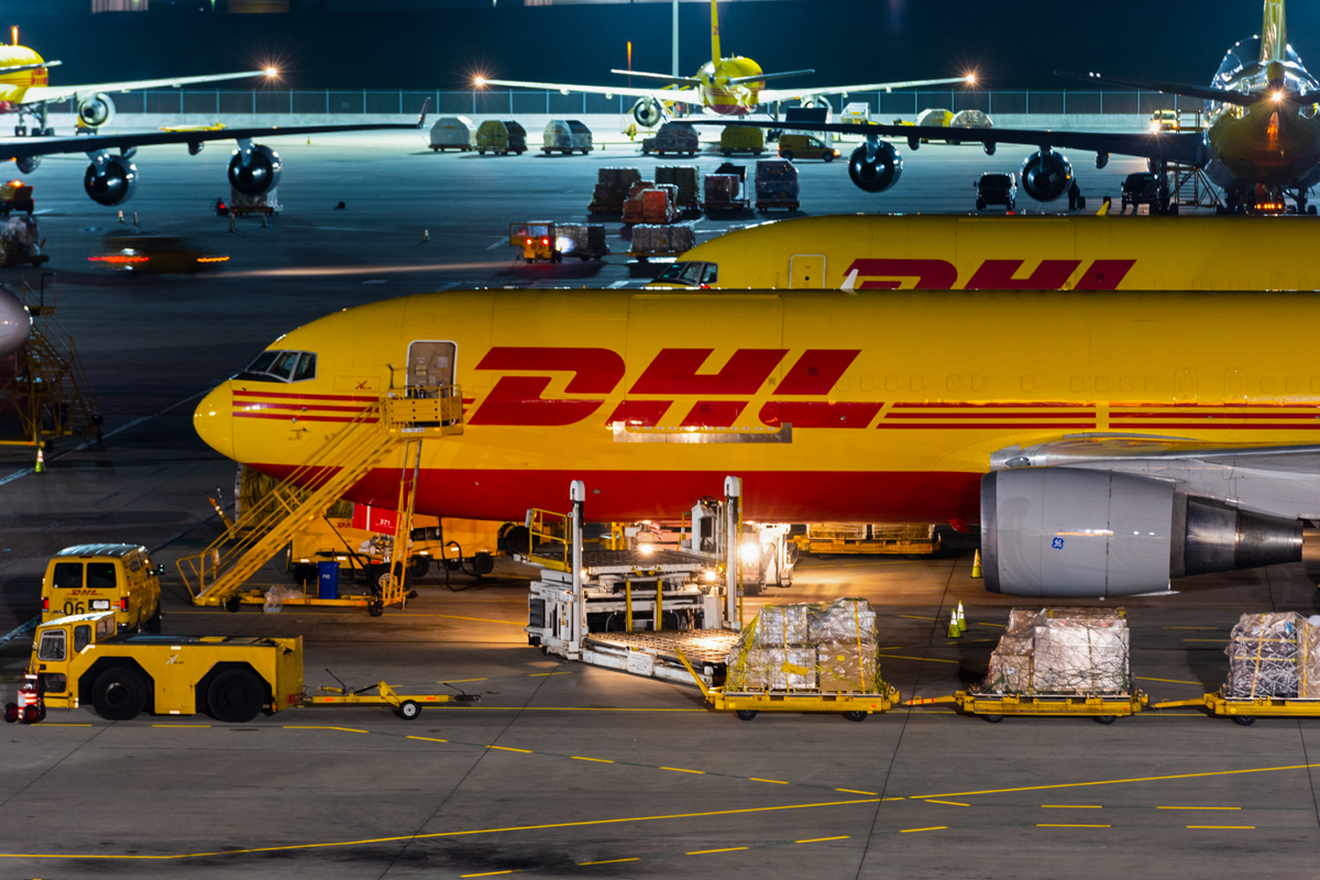 Yellow DHL airplane on tarmac being loaded with crates.